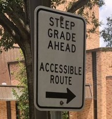 A traffic sign reads steep grade ahead, accessible route, with an arrow pointing to the right.